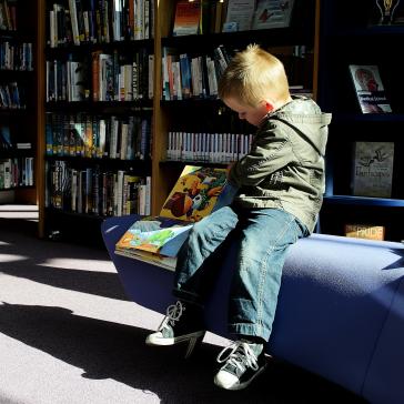Bild eines Jungen vor Bücherregalen, der sich ein aufgeschlagenes Buch ansieht